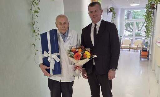 doktor Tadeusz Beszta Borowski i burmistrz Łap krzysztof Gołaszewski z kwiatami i prezentem na korytarzu hospicjum