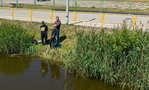 Dwoje dorosłych i chłopiec stoją nad wodą na brzegu i chłopiec łowi ryby na wędkę